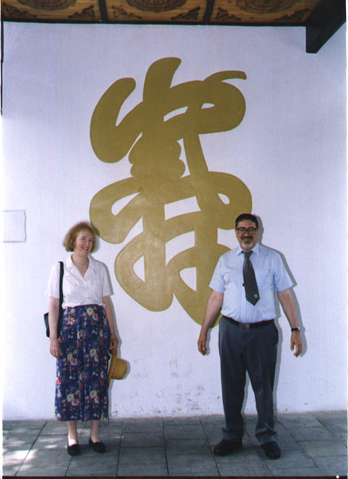 Dick and his wife, Susan, posing in front of a wall with a Chinese character on it in China